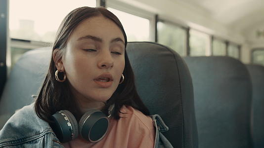 体贴的女孩坐在公共汽车上戴着耳机视频的预览图