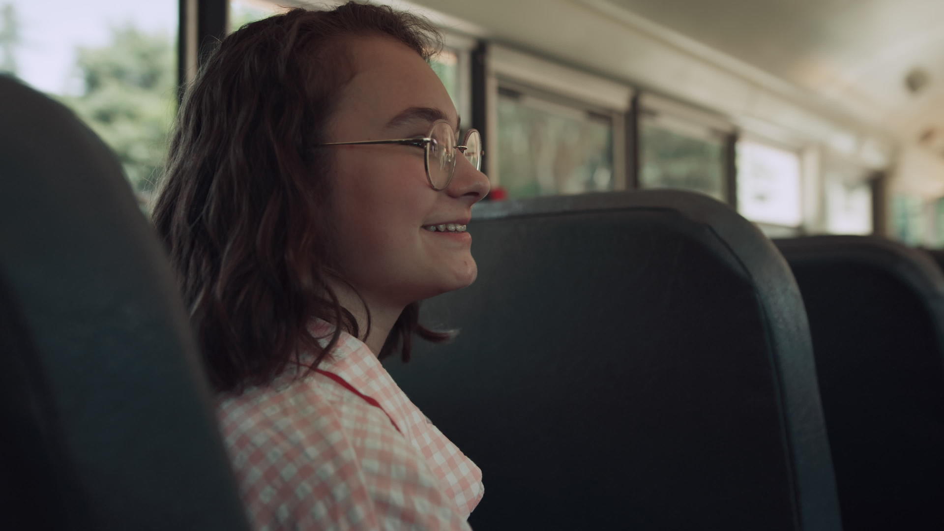 一个微笑的女孩坐在校车上和朋友聊天视频的预览图