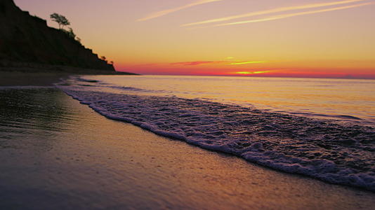 宁静的海岸线和山丘在明亮的橙色夕阳下剪影视频的预览图