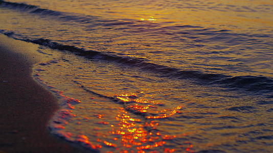 在金色的夕阳下温暖的海水在黑暗的沙滩上飞溅视频的预览图