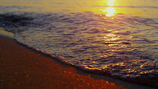 在橙色的日落黄昏特写海浪以缓慢的动作打破沙滩视频的预览图