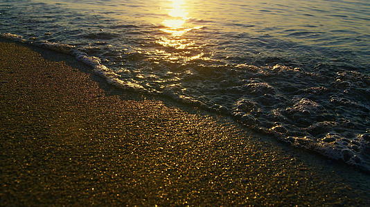 黄金日出时海浪溅起沙滩的太阳光反射视频的预览图