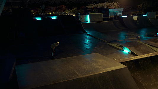 年青的滑冰者在夜间滑板公园的坡道上表演滑板技巧视频的预览图