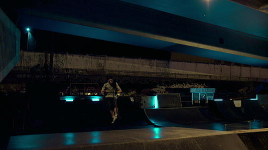 在夜间滑板公园坡道上活跃的青少年骑滑板车视频的预览图
