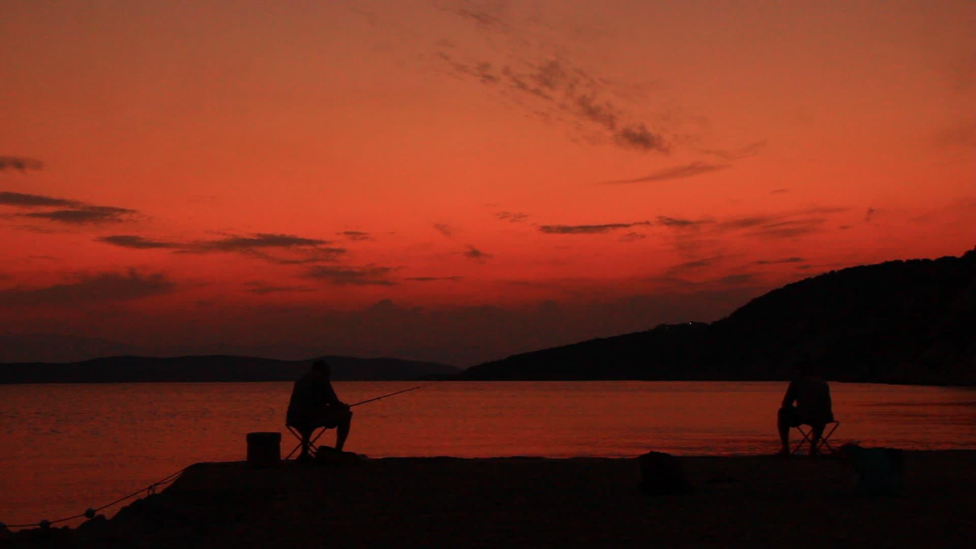日落时在岸上钓鱼的渔民视频的预览图