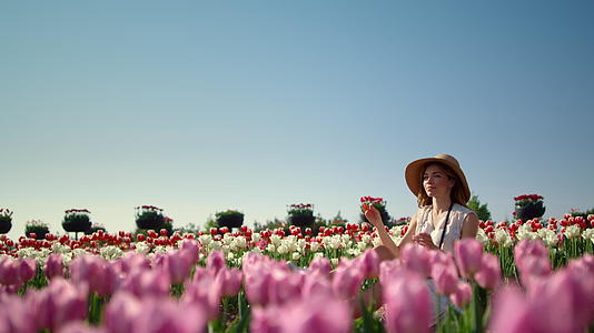 年轻而温柔的女人戴着帽子在盛开的花景中享受阳光视频的预览图