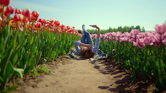 郁金香在阳光明媚的日子里看着手机屏幕上的春天女孩视频的预览图