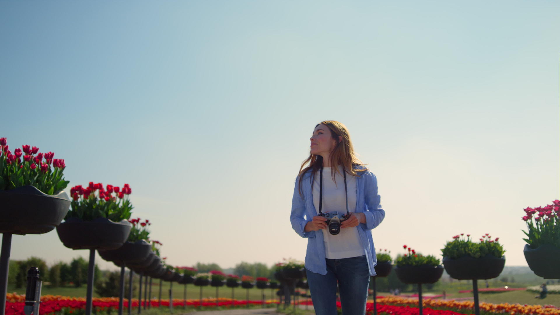 阳光明媚的日子里快乐的女摄影师在盛开的公园里慢慢奔跑视频的预览图