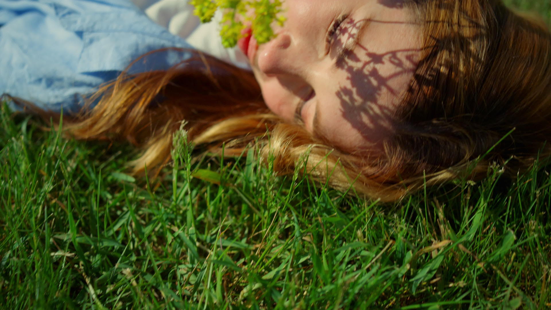 轻松的redhar女性用春花抚摸着自己的脸在绿草的背景下抚摸着自己的脸视频的预览图