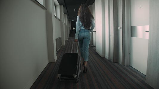 年轻女子在酒店走廊里拉着行李箱视频的预览图