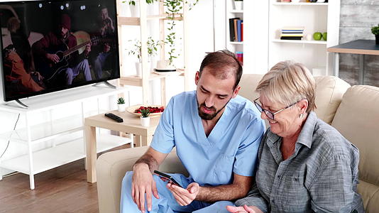 养老院的男护士帮助老年妇女使用手机视频的预览图