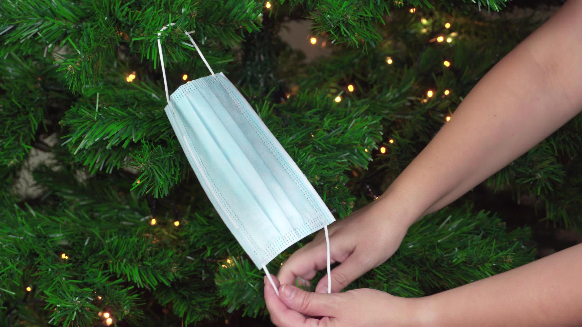 圣诞节用口罩作为装饰挂在绿树上灯光照亮视频的预览图