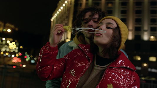 夫妻俩在户外吹香皂泡在城市街道上愉快地约会视频的预览图