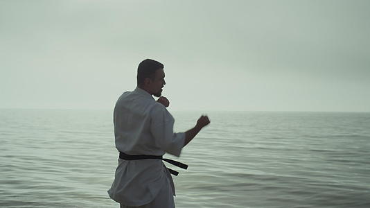 强壮的男人在海边练习跆拳道在多云的天空中慢慢移动视频的预览图