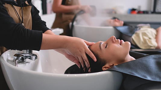 美容院的理发师在美女洗头时给顾客按摩头发她看起来轻松愉快视频的预览图