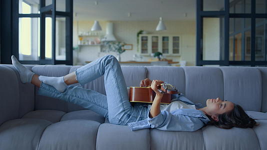 女孩在客厅弹吉他女人带着乐器躺在沙发上视频的预览图