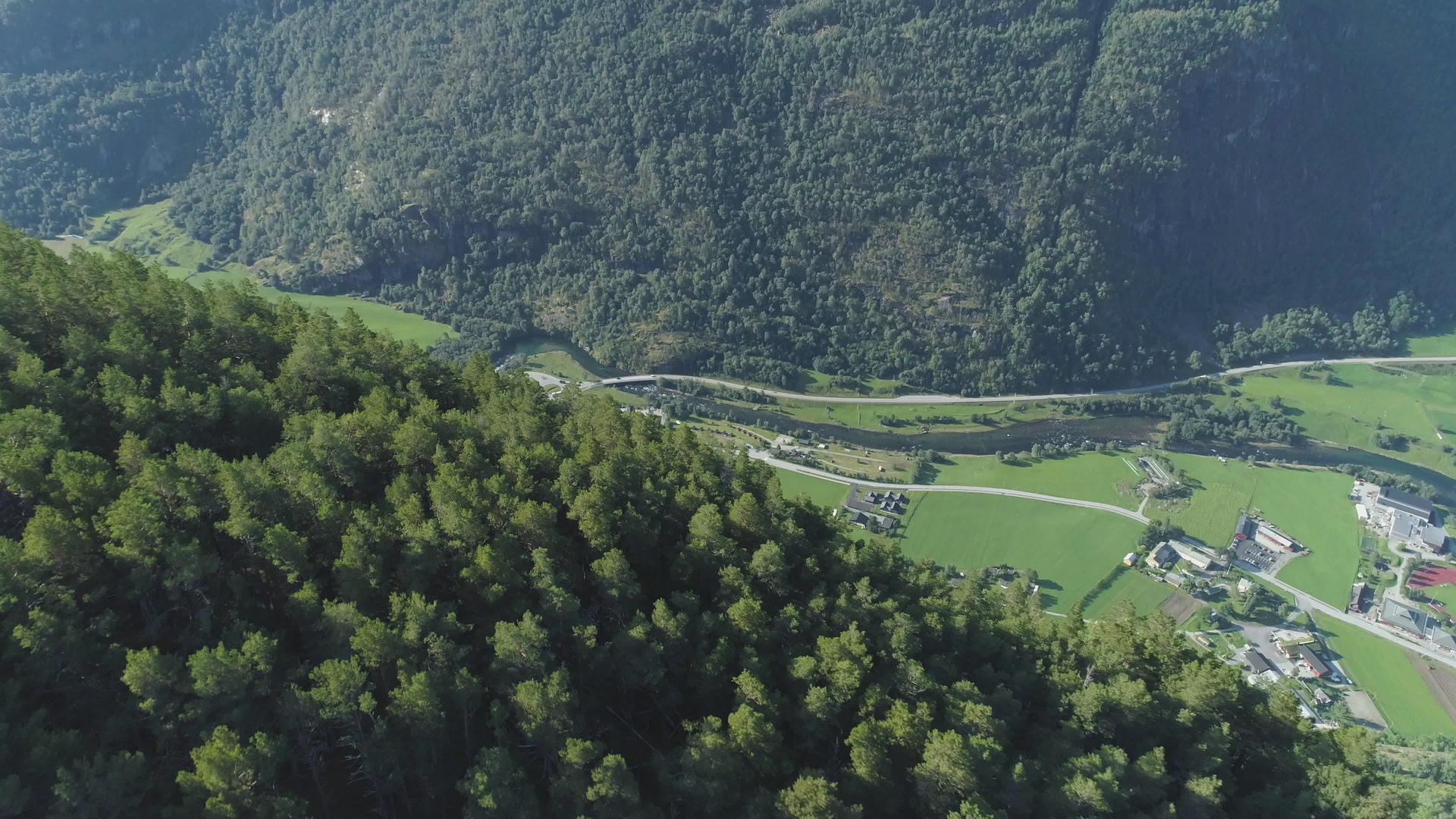 无人机在阳光明媚的夏天飞越挪威的绿树和村庄的山坡视频的预览图