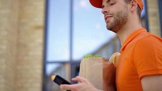 快递员带着纸袋和手机外出送食物的人视频的预览图