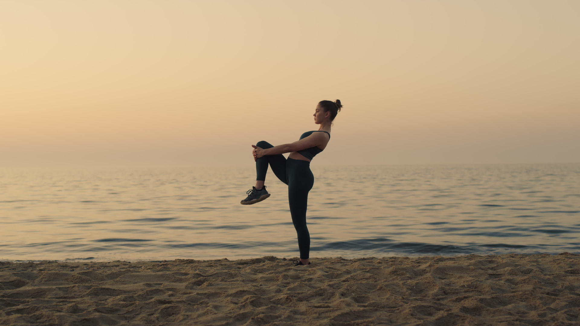 运动女孩抱着膝盖在沙滩上伸展双腿视频的预览图