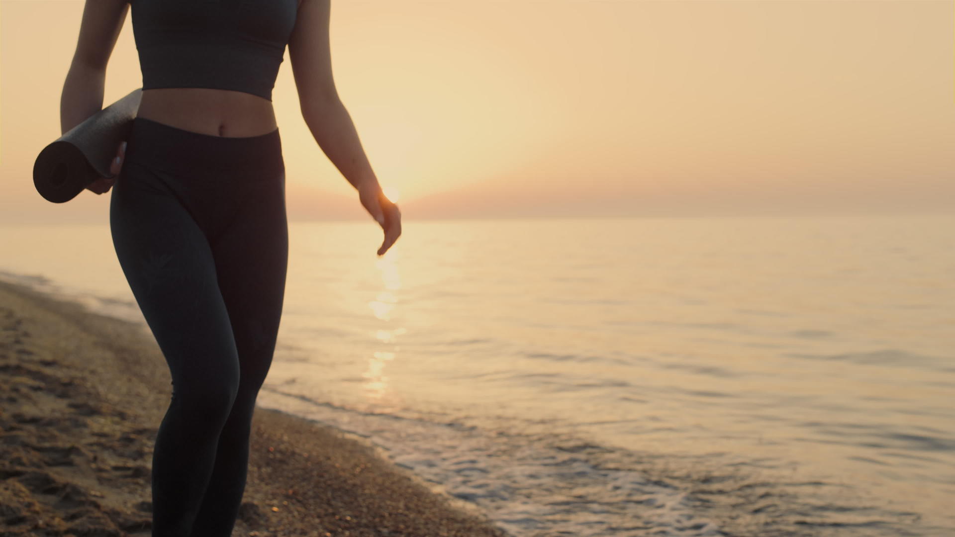 日落时运动女子拿着运动垫走在沙滩上视频的预览图