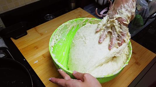 年轻女性在家里的绿色碗里用手揉面包和面团人们在家里视频的预览图