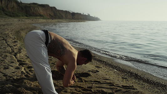 强壮的男人弯腰在沙滩上伸展视频的预览图