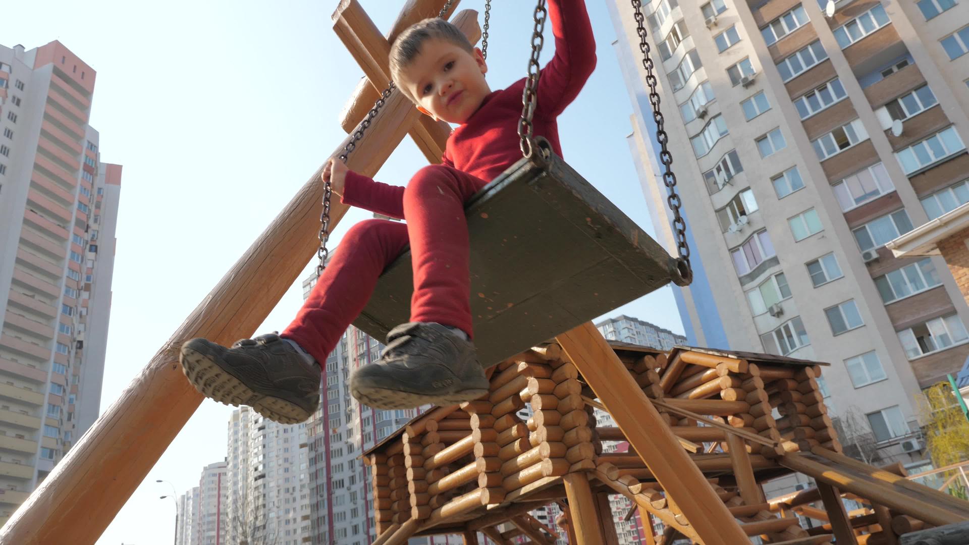 男孩在摩天大楼附近的木制操场上穿着红色西装在木头上摇摆视频的预览图