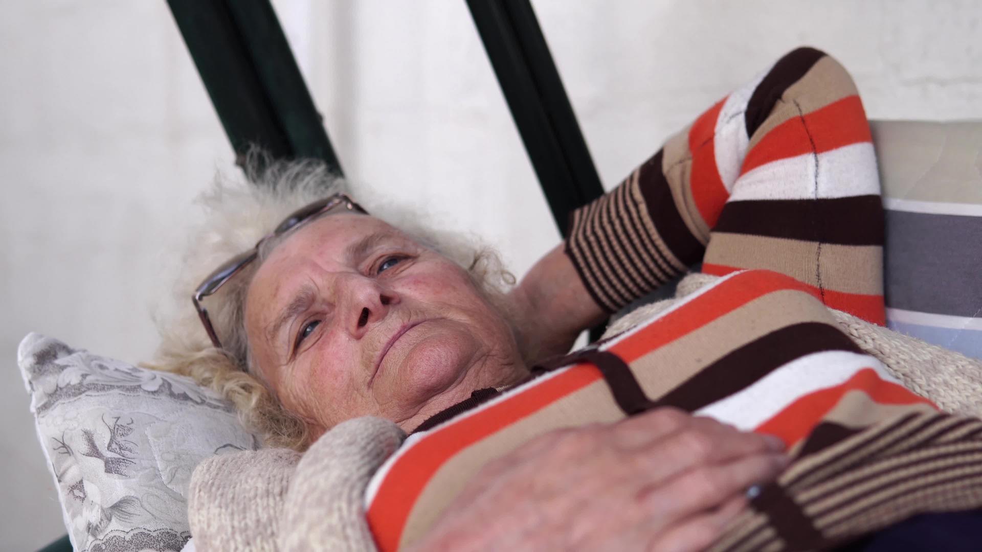 美丽的老年妇女肖像躺在户外门廊摇摆和思考视频的预览图