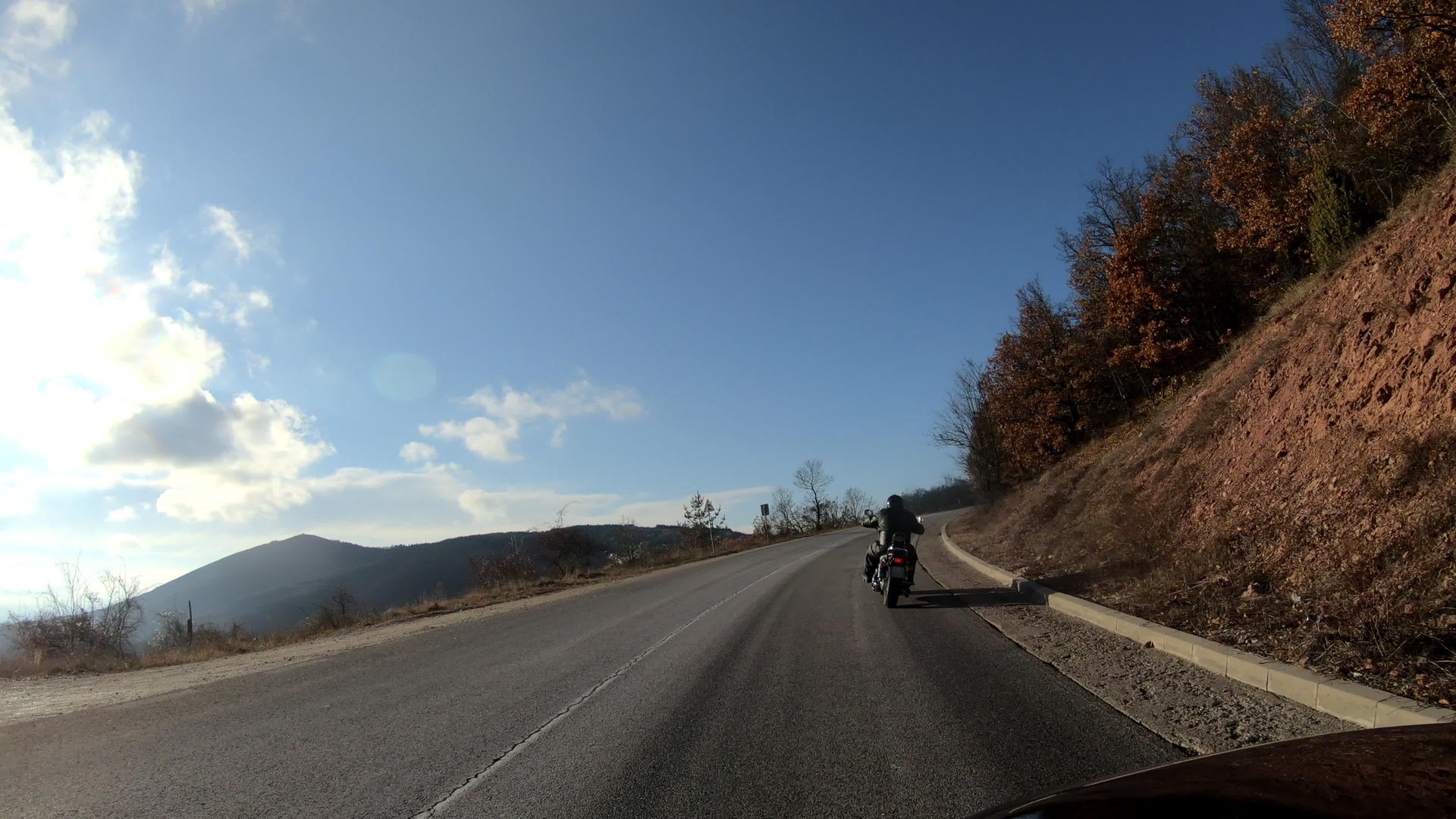 一名身穿黑色皮夹克的男子在山对面的路上骑着摩托车视频的预览图