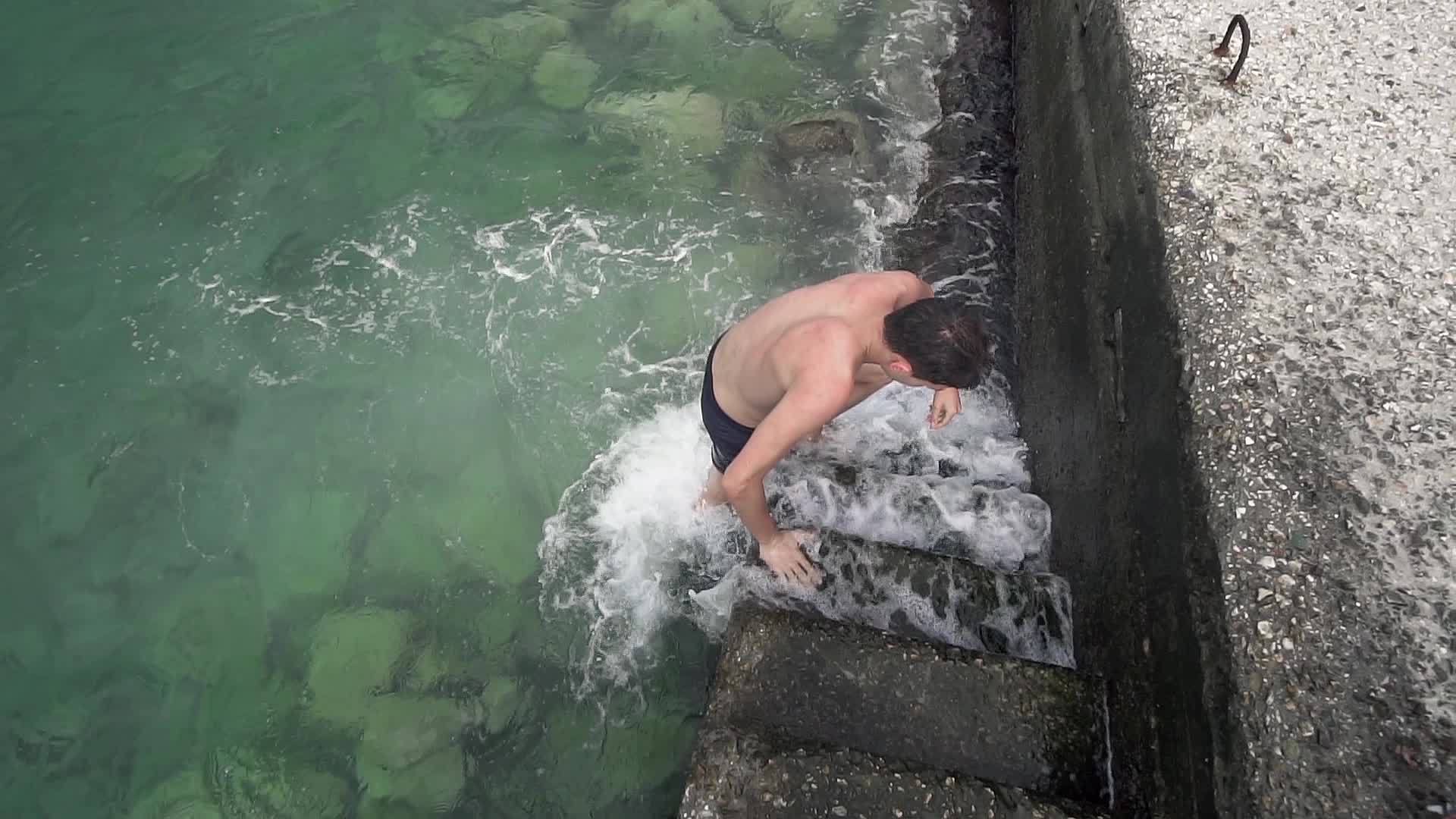 帅帅的男孩从港口楼梯上的海水中慢慢出来视频的预览图