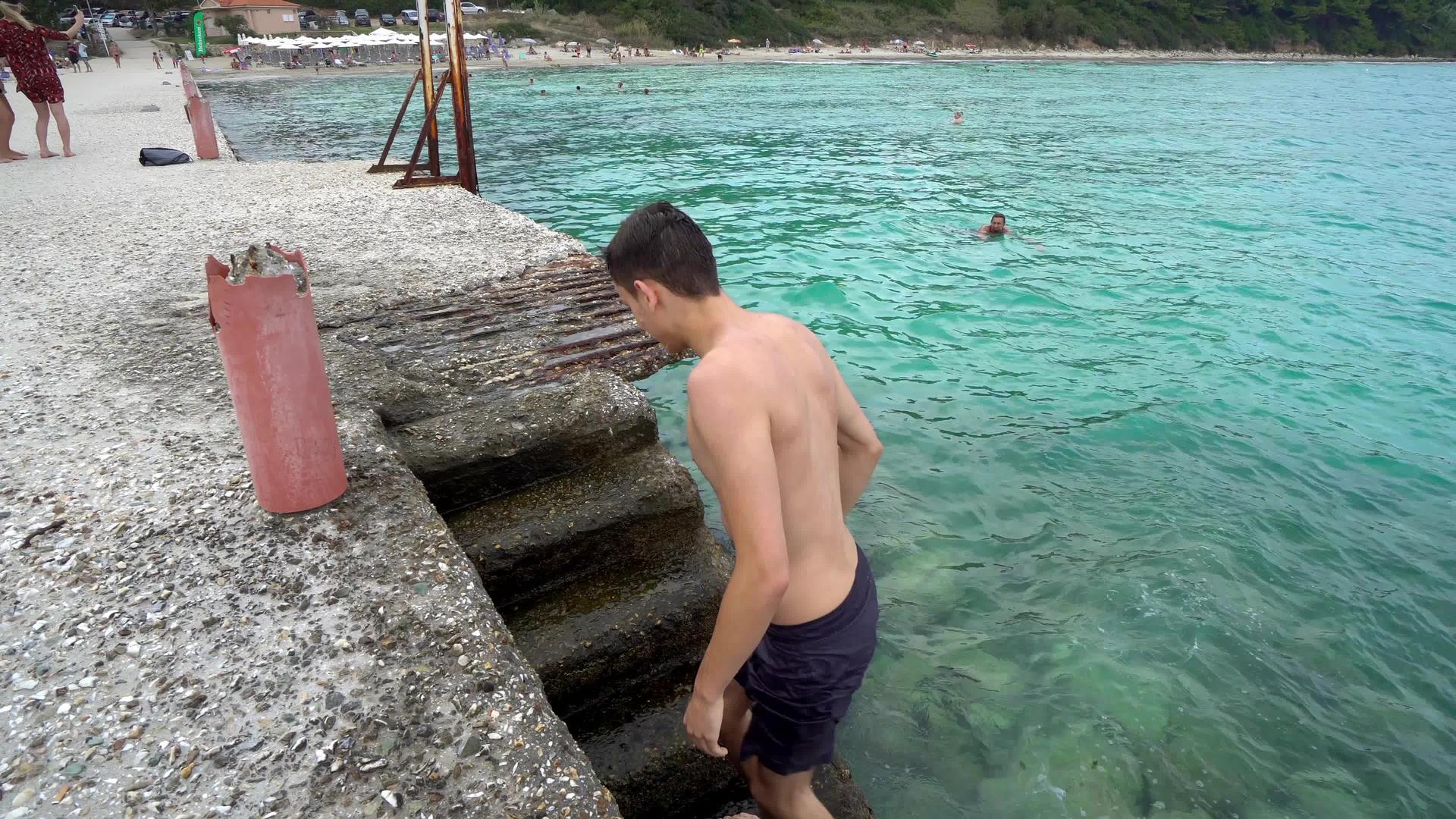 英俊的男孩从港口楼梯的海水中出来视频的预览图