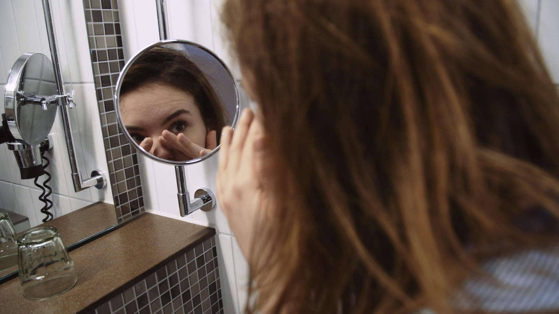 年轻女性用放大的浴室镜检查脸部视频的预览图
