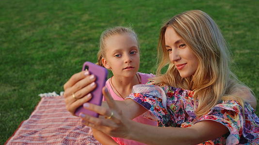 母亲和女儿在公园里摆姿势家庭成员在户外手机上自拍视频的预览图