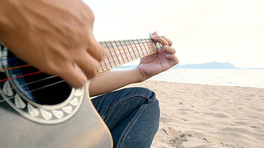 4k日落时关闭一个在沙滩上弹吉他的人的近距离感觉视频的预览图