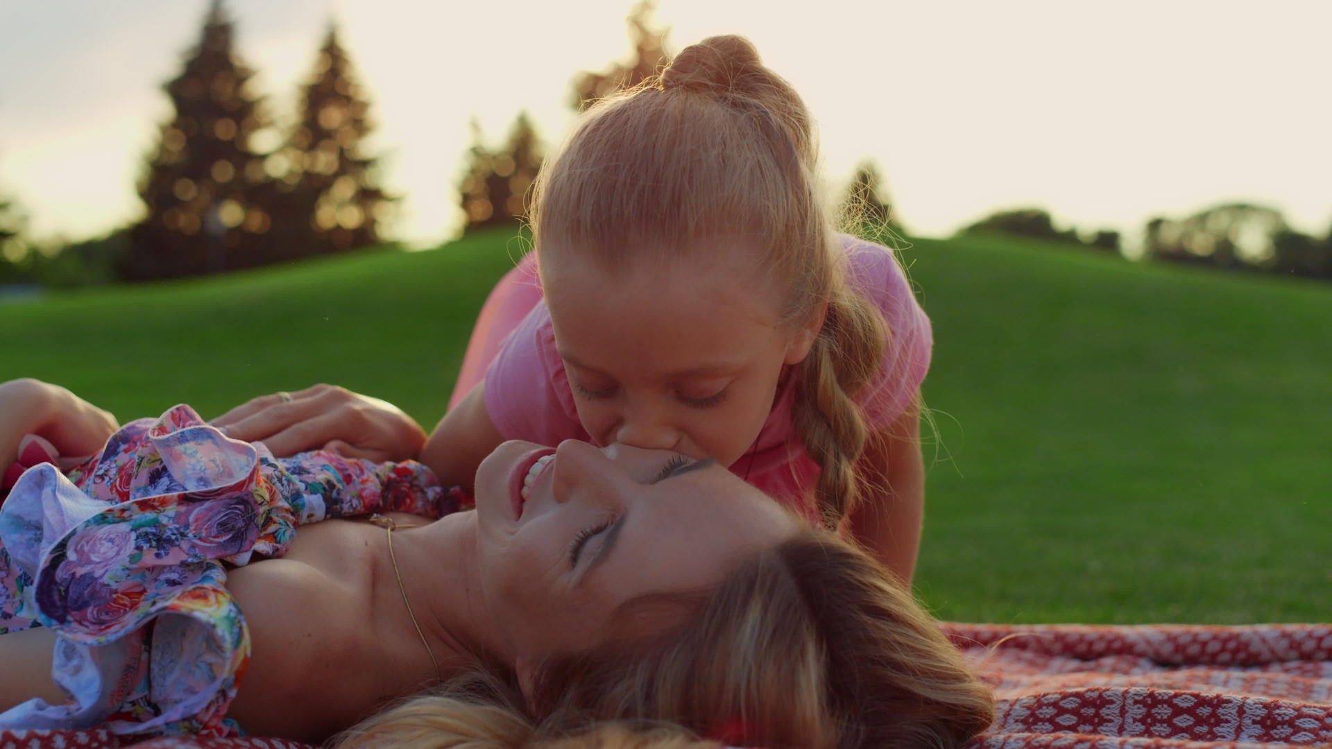 女人和孩子在草地上微笑女儿在市公园亲吻母亲视频的预览图