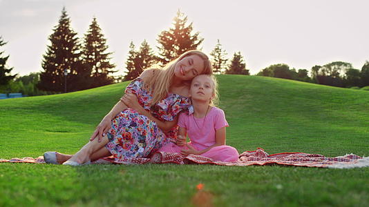 日落时家庭在草地上摆姿势女人在城市公园拥抱女孩视频的预览图