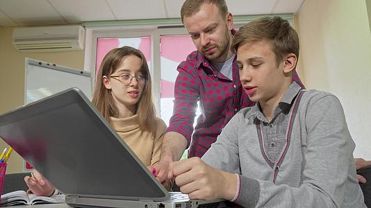 成年男教师使用笔记本电脑帮助他们的学生从事任务视频的预览图