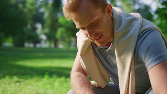 特写帅气的男人坐在夏天的公园里蹲下来抚摸动物视频的预览图