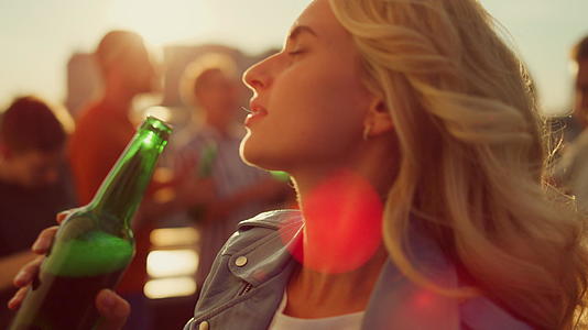 年轻女子在日落屋顶上喝啤酒视频的预览图