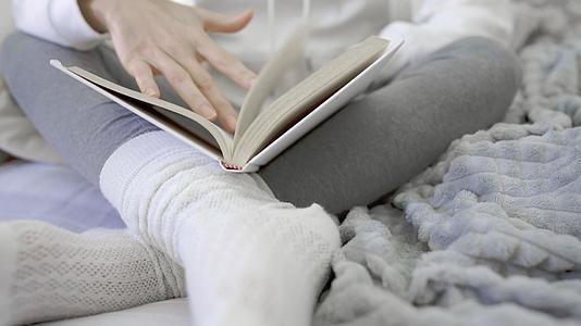 一个面目全非的年轻女子盘腿坐在沙发上看书靠在白色羊毛袜子上视频的预览图