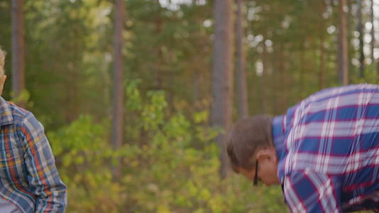 旅行的父亲和年轻人在夏天的林地里用斧头砍柴而他的父亲则用斧头砍柴视频的预览图