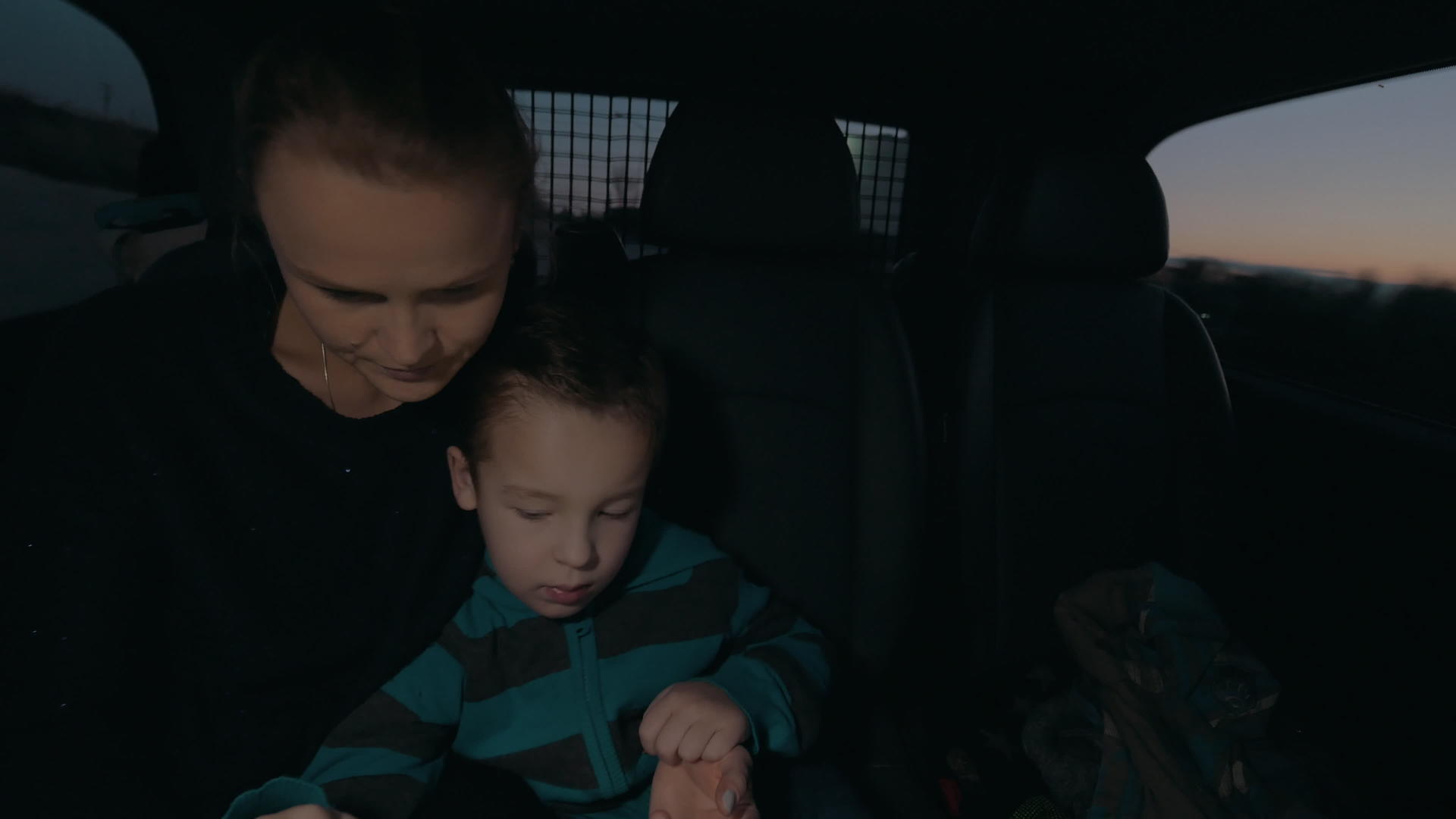 一个带着儿子的女人在黑暗中坐在后座的车里看着电脑平板电脑视频的预览图