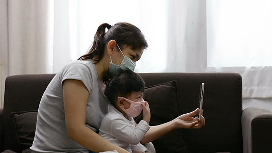 戴着面具的亚洲母亲和女儿在视频通话中用电话交谈视频的预览图