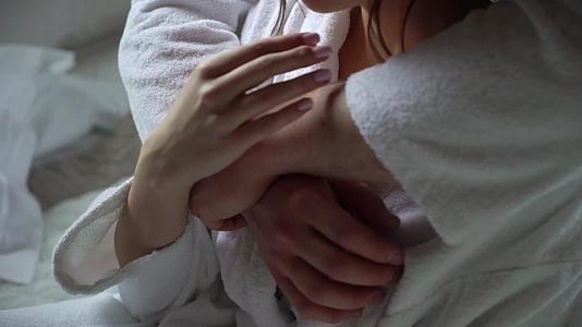 年轻夫妇穿着浴袍坐在床上拥抱握手视频的预览图