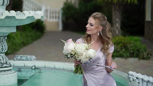 年轻的金发女子穿着内衣在喷泉附近的花园里披着新娘视频的预览图