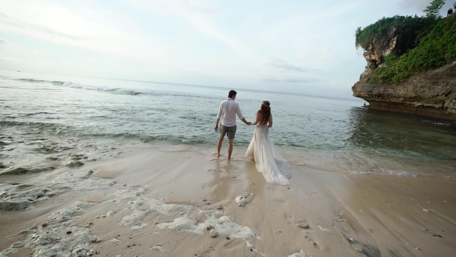 新婚夫妇在傍晚或日落时分在海滩上散步手牵手拥抱视频的预览图