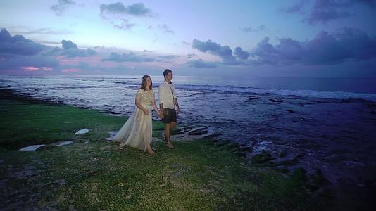 新婚夫妇在傍晚或日落时分在海滩上散步手牵手拥抱视频的预览图