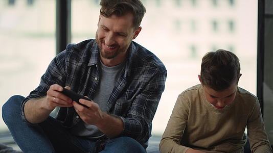 父亲和儿子在家用智能手机玩游戏视频的预览图