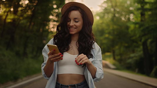 微笑的女人在公园里通过电话发短信视频的预览图