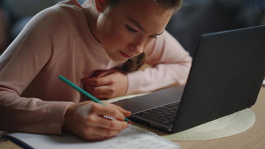 女学生在室内笔记本电脑旁做作业在家学习的未成年女孩视频的预览图